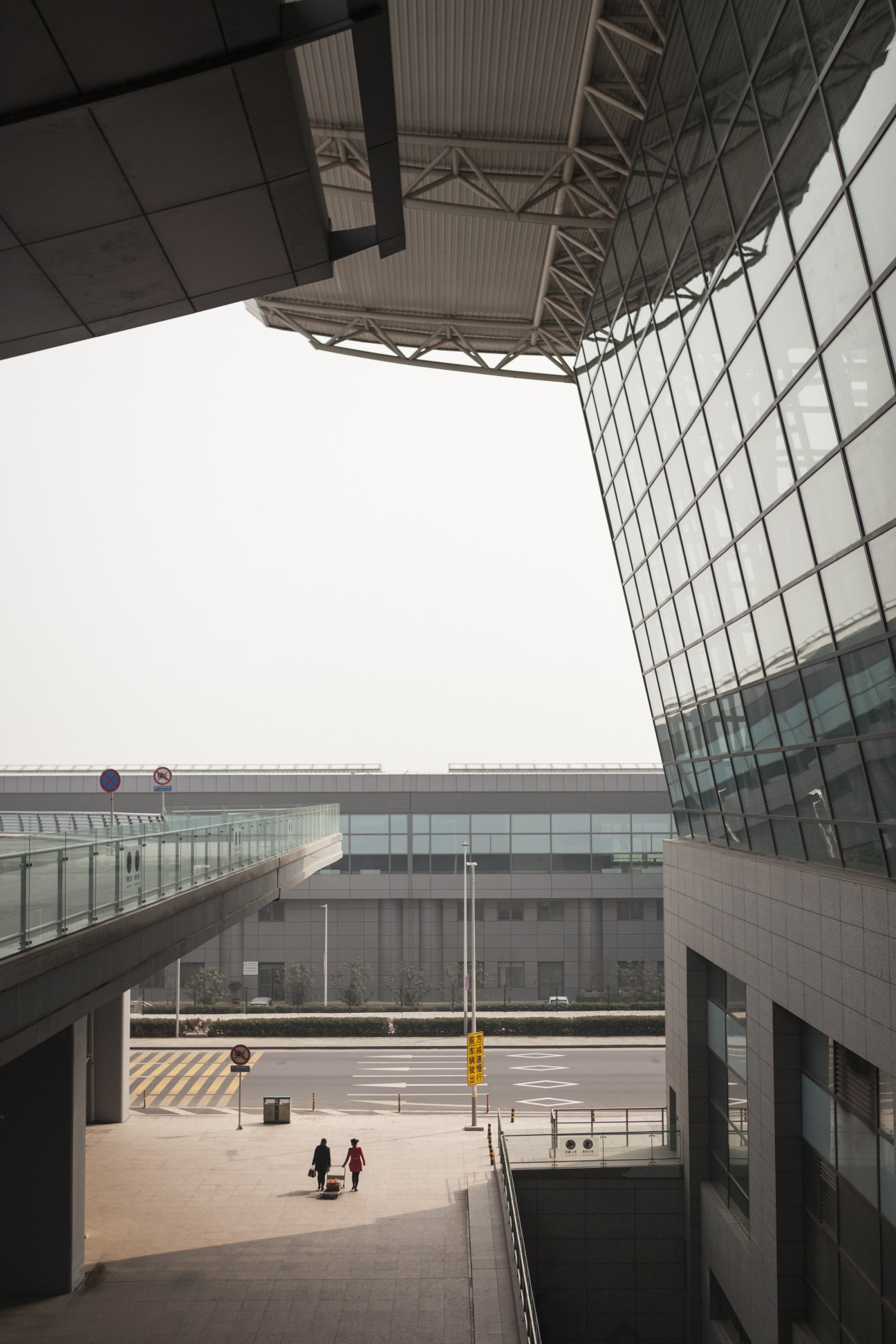 View from elevated departures level at Xi'an Xianyang International Airport Terminal 3, showing modern architecture with glass and steel framework overlooking an empty plaza below.