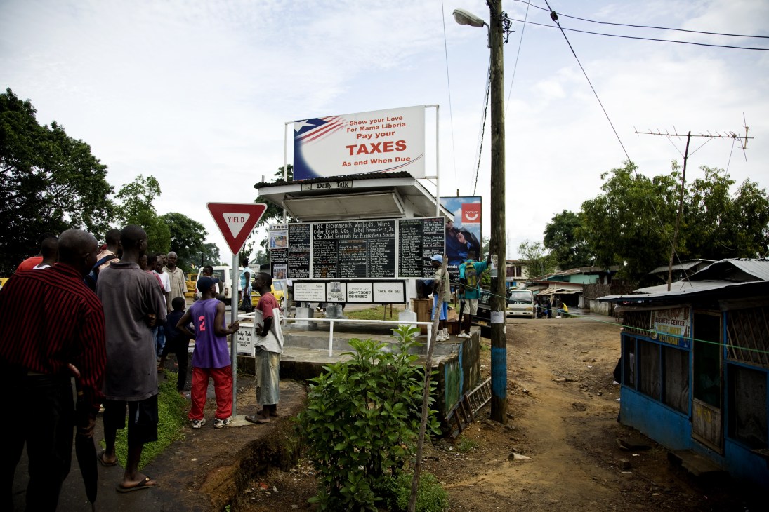 People gather around Alfred Sirleaf's Daily Talk blackboard newspaper in Monrovia, Liberia, displaying chalk-written news stories.