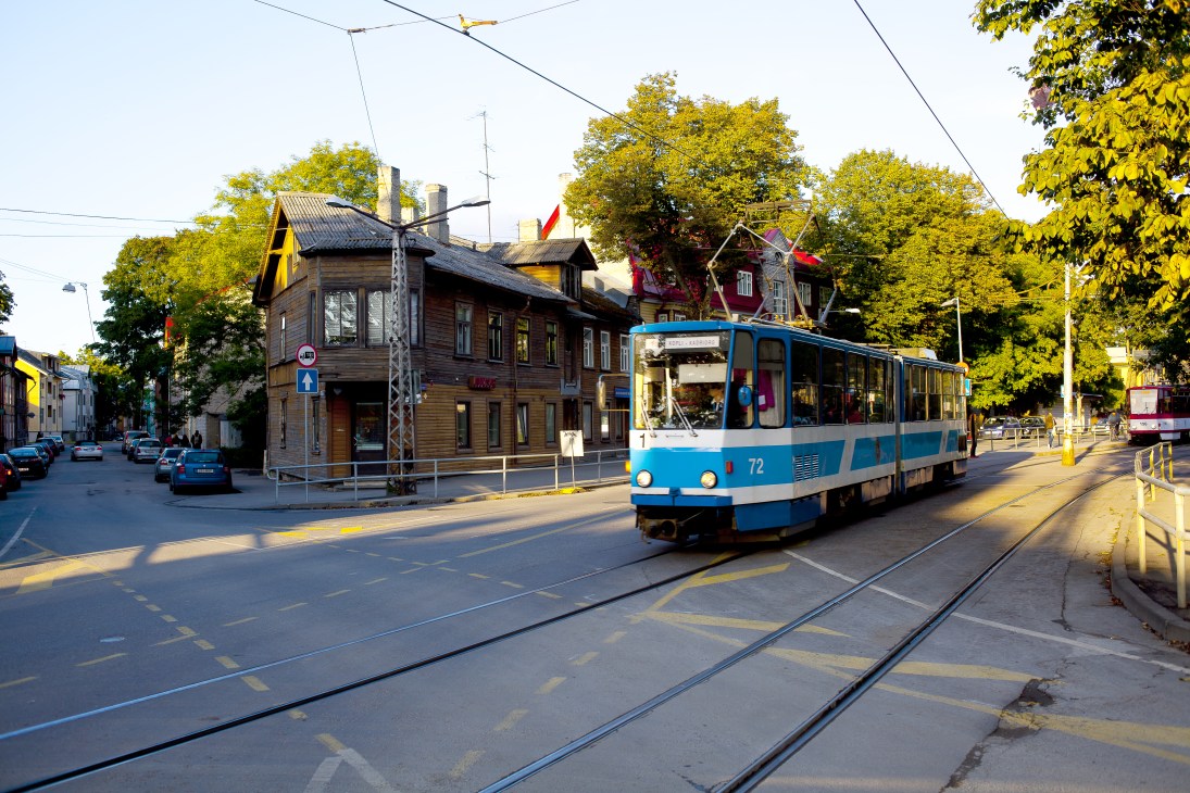 Blue and white tram number 72 traveling on tracks through Kalamaja, passing traditional wooden buildings.