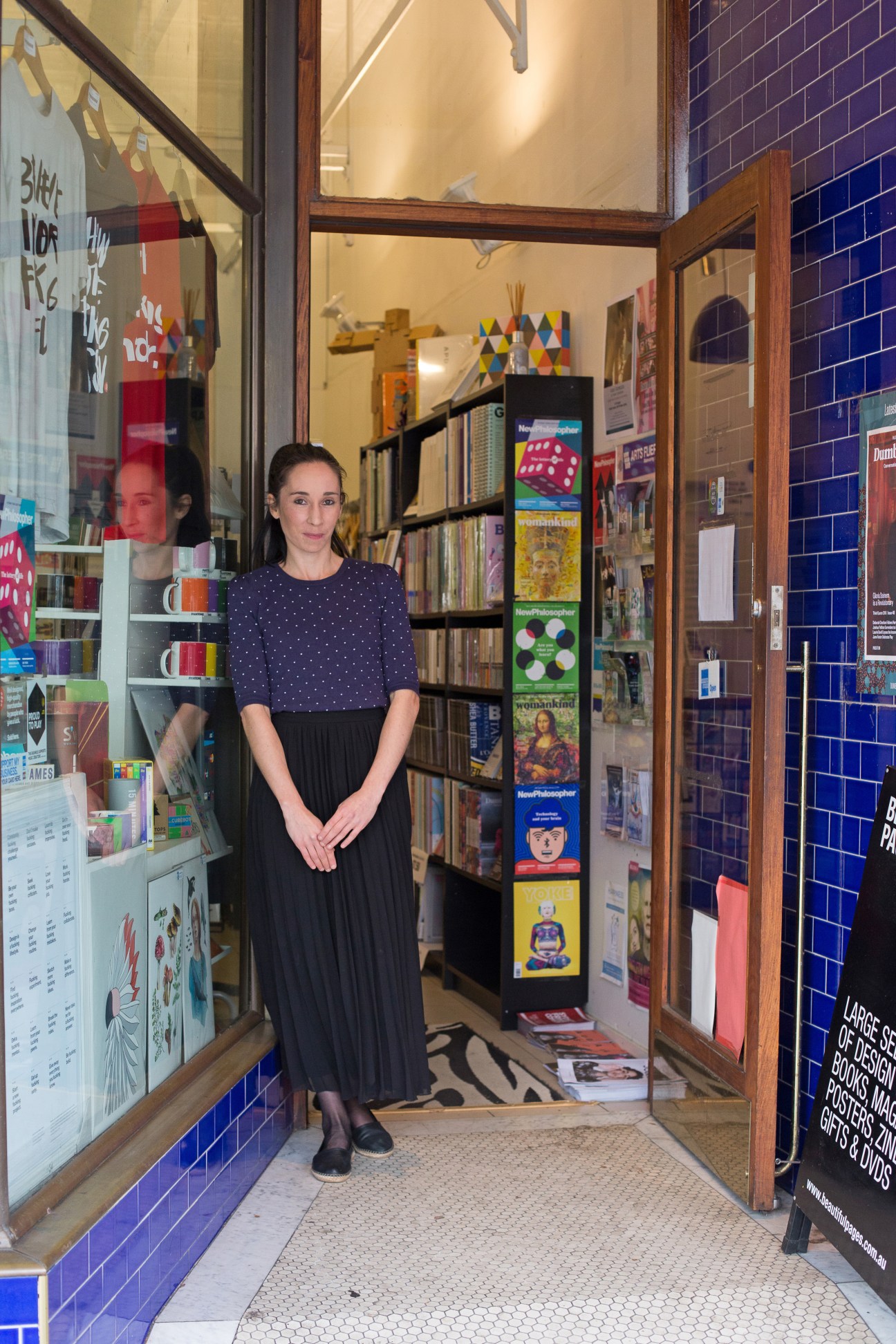 Woman standing in doorway of Beautiful Pages bookshop in Sydney, with shelves of books and magazines visible inside.