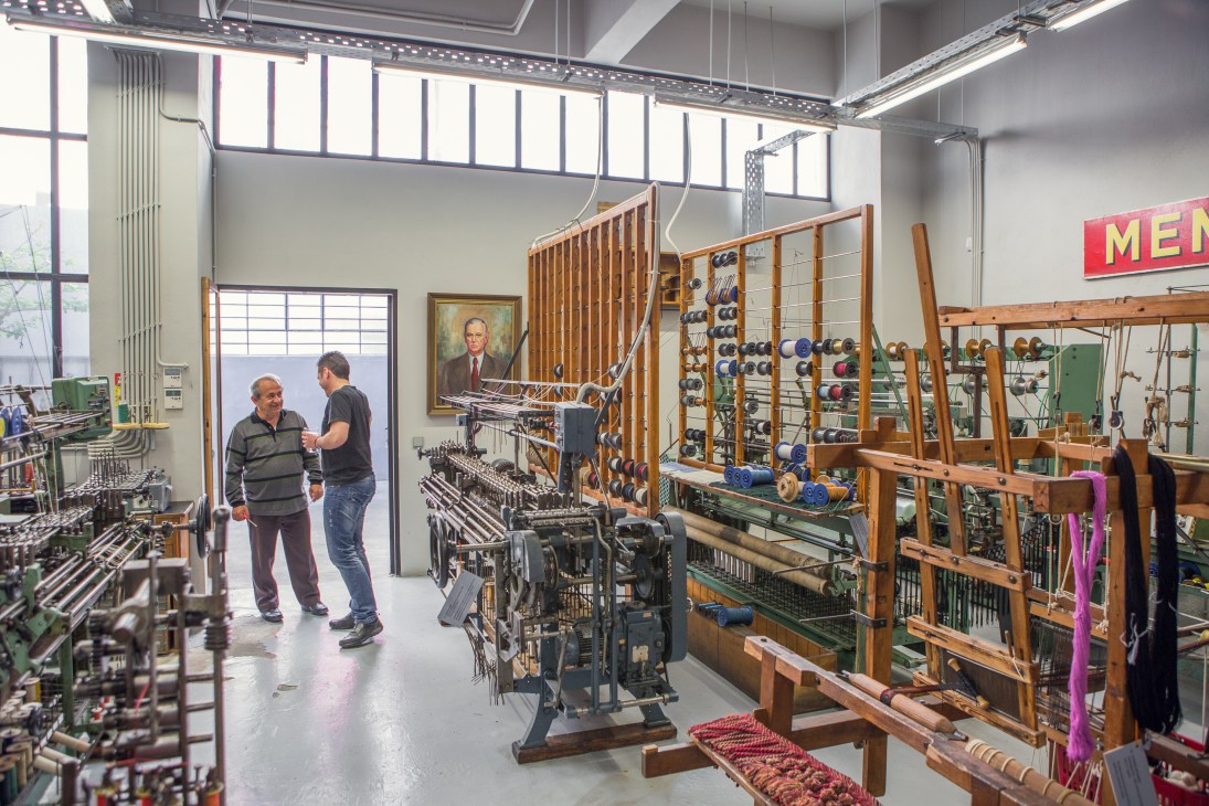 Interior of Mentis yarn factory showing traditional wooden looms and spools of colored thread.