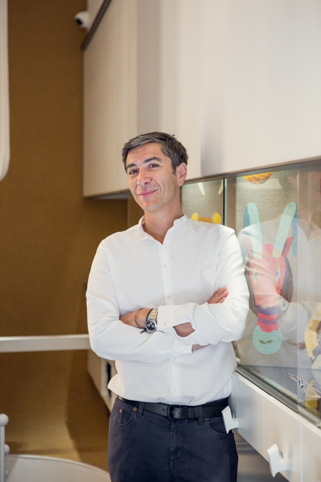 Yannis Sergakis stands in his Athens boutique next to a display case of colorful jewelry pieces.