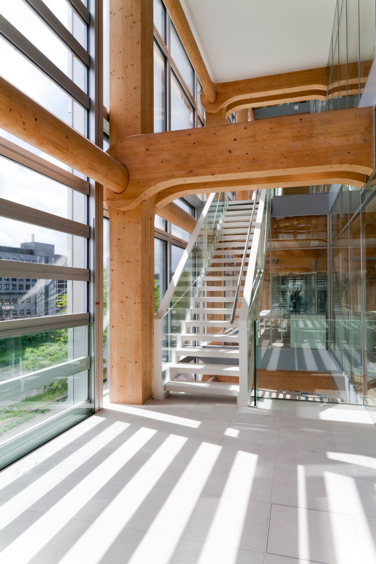 Interior view of Tamedia building showing exposed Austrian spruce timber beams, large windows, and a glass staircase with natural light.
