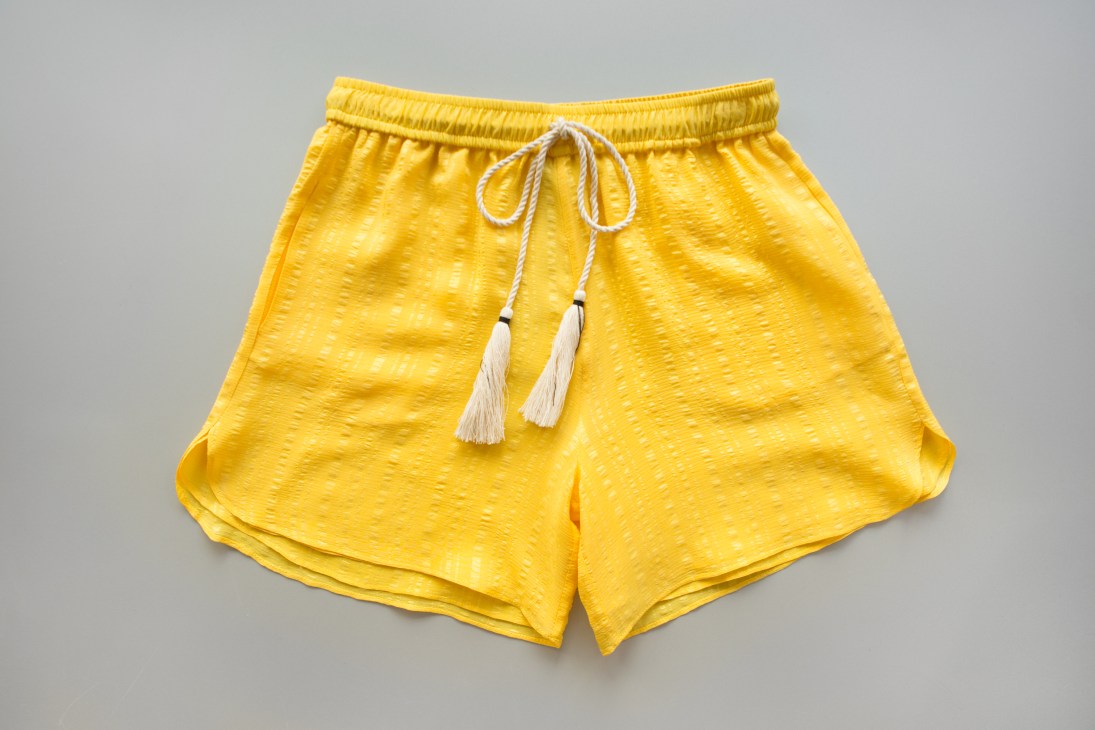 Yellow shorts made from Soufli silk with white drawstring ties on gray background
