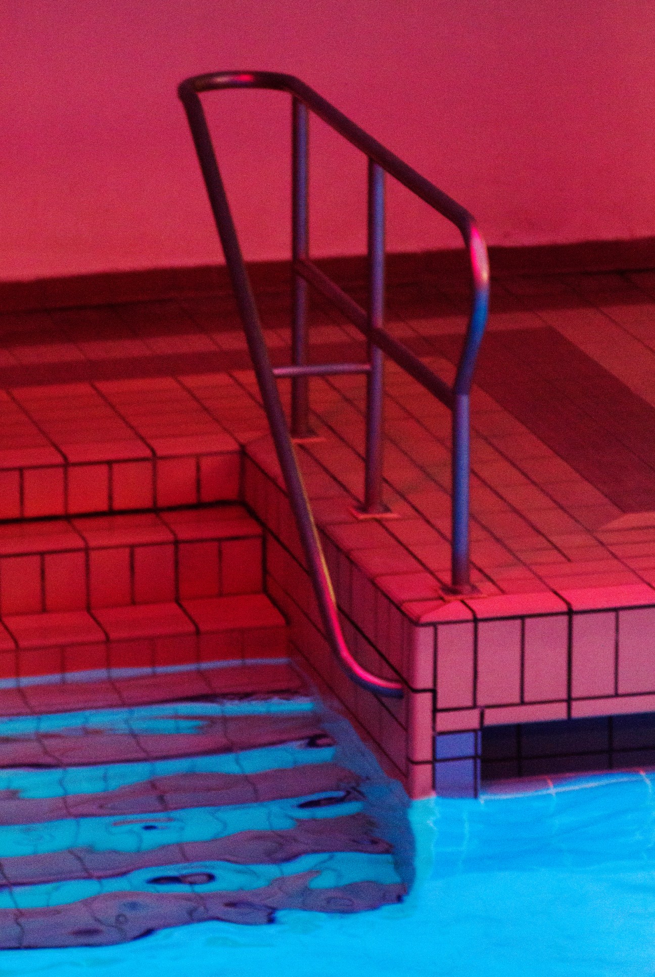 Neon-lit swimming pool with stairs and lane dividers at La Piscine de Pontoise in Paris.