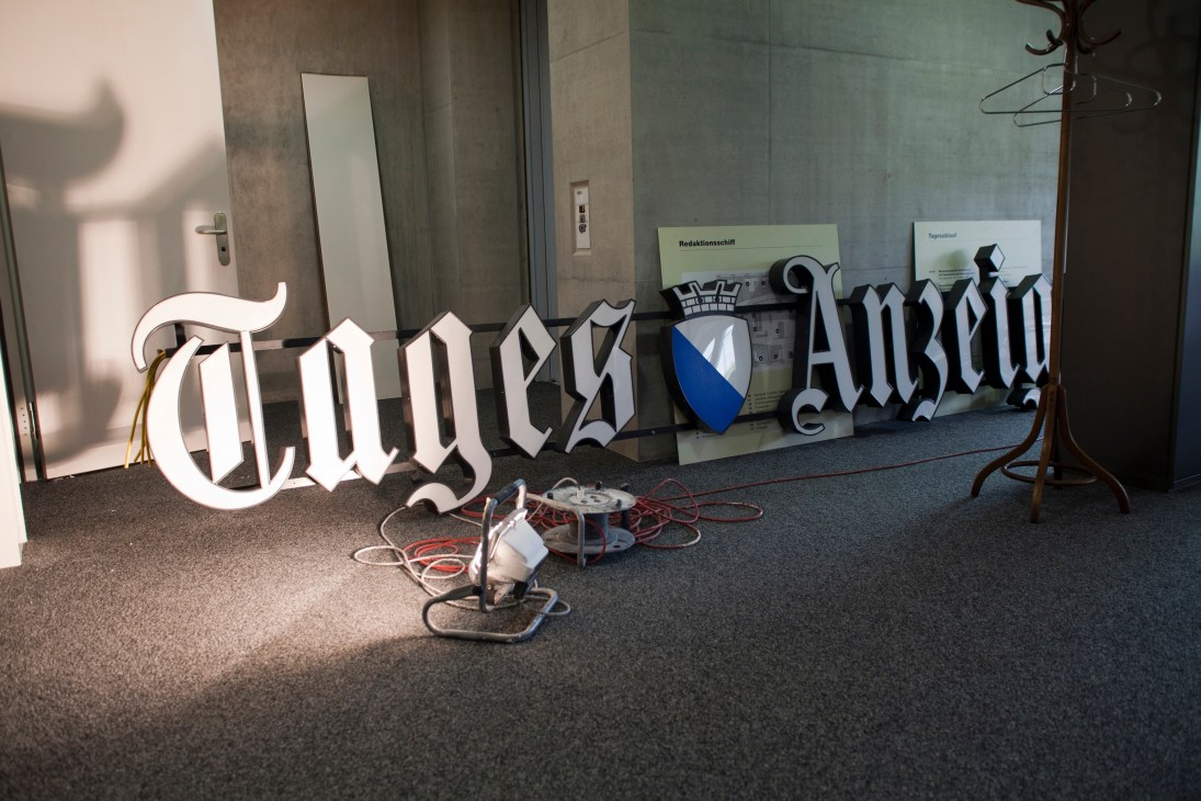 Illuminated neon Tages-Anzeiger newspaper sign with coat hangers and cables in an empty room.