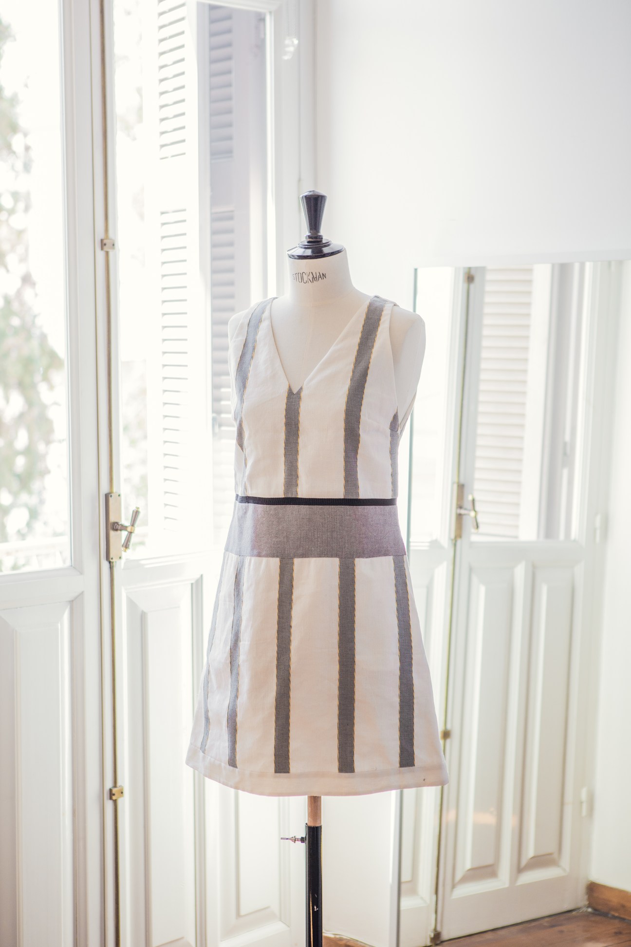 Sleeveless linen dress with vertical stripes displayed on a dress form near bright windows.