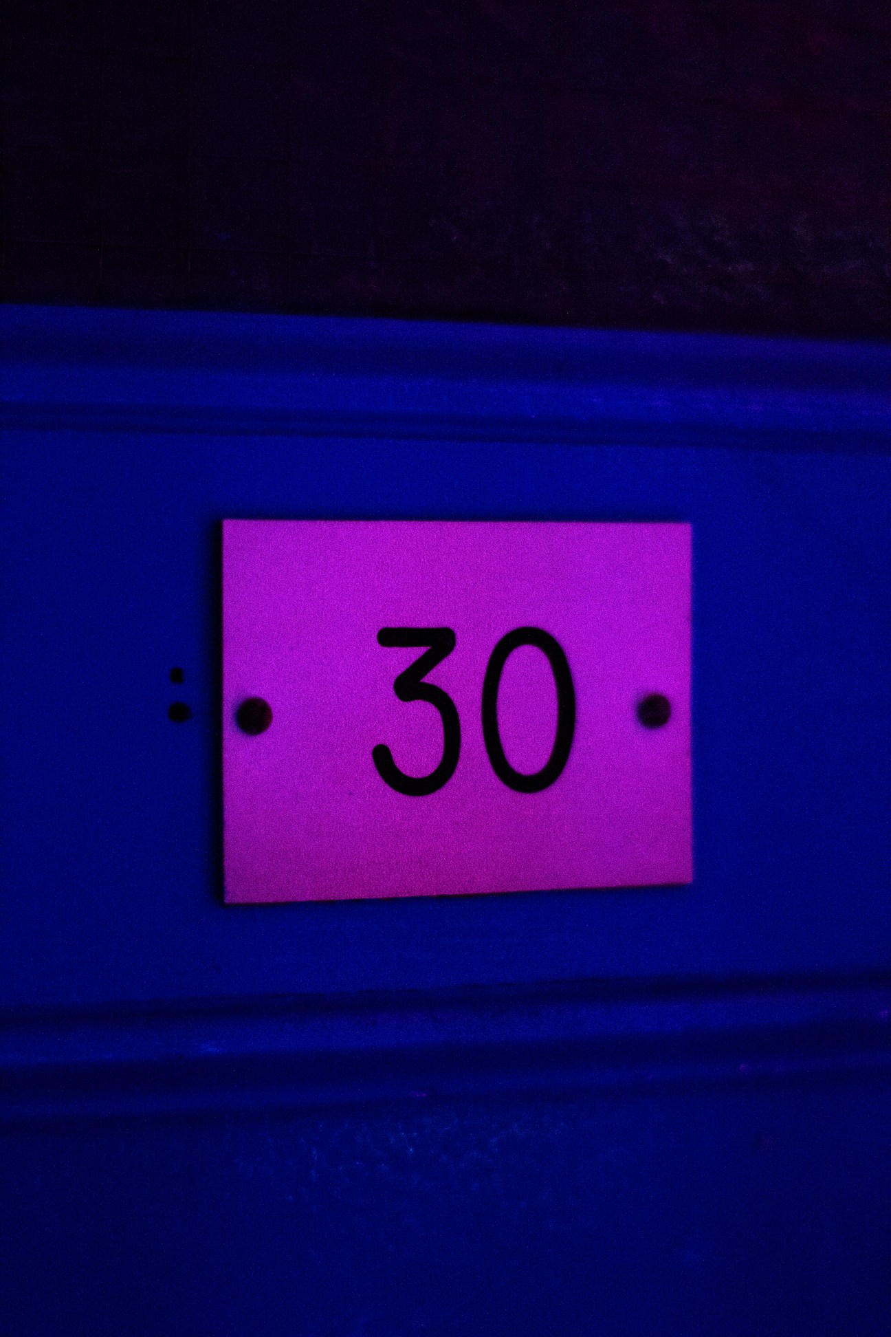 A bright magenta numbered cabin door labeled 30 mounted on a blue wall at La Piscine de Pontoise in Paris.