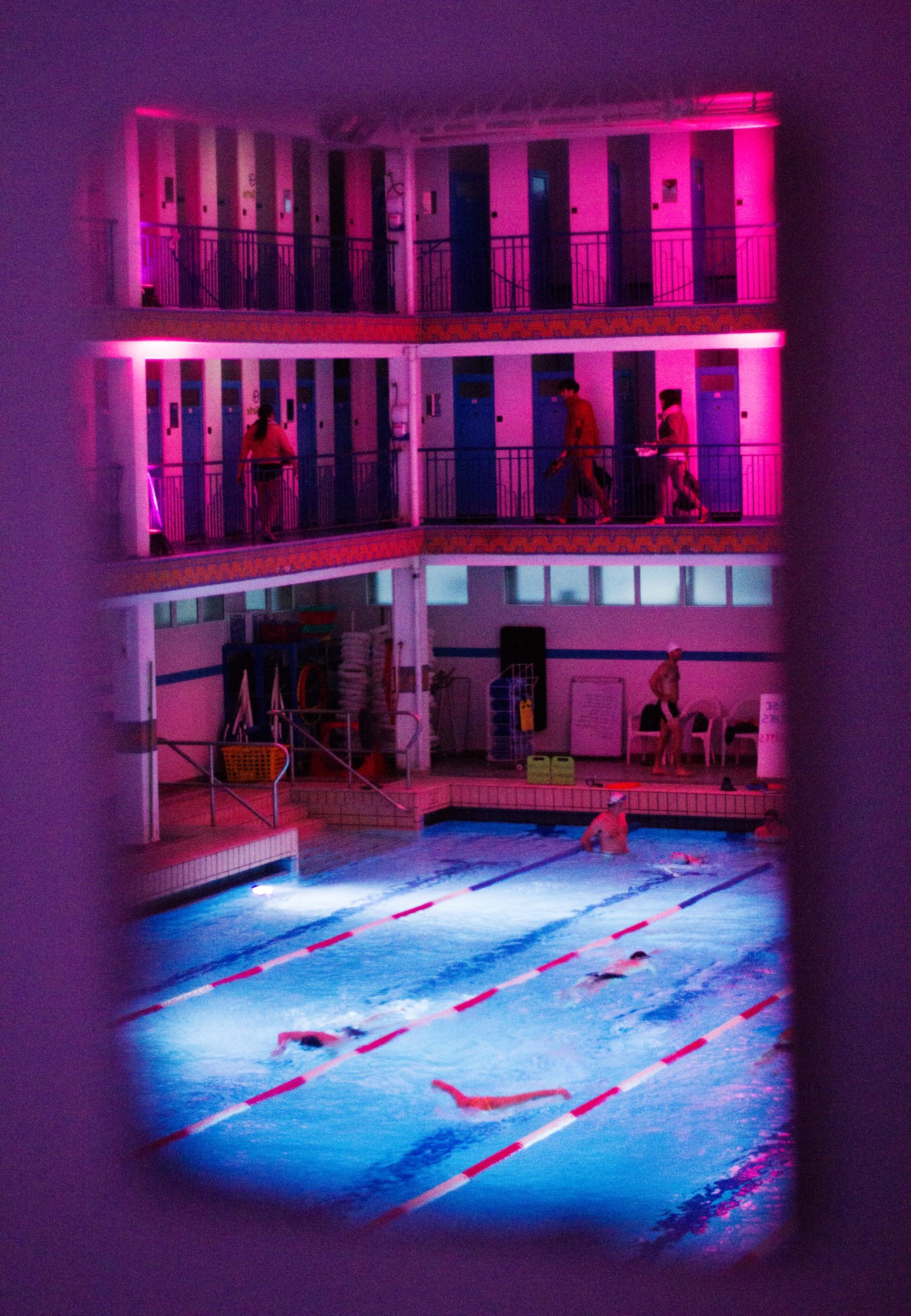 La Piscine de Pontoise lit with vibrant neon pink and blue lights at night, showing the pool and multi-story cabin galleries.