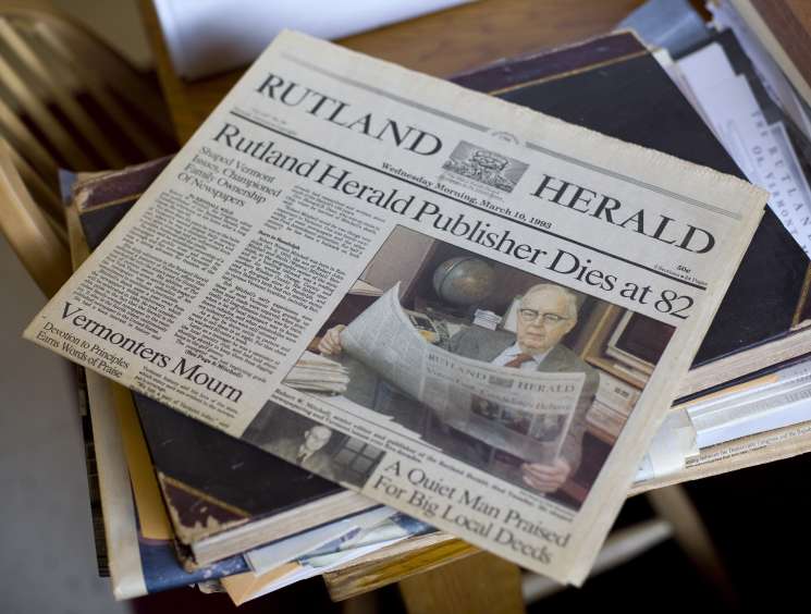 Rutland Herald newspaper front page with headline about publisher's death, showing archival copies stacked together.