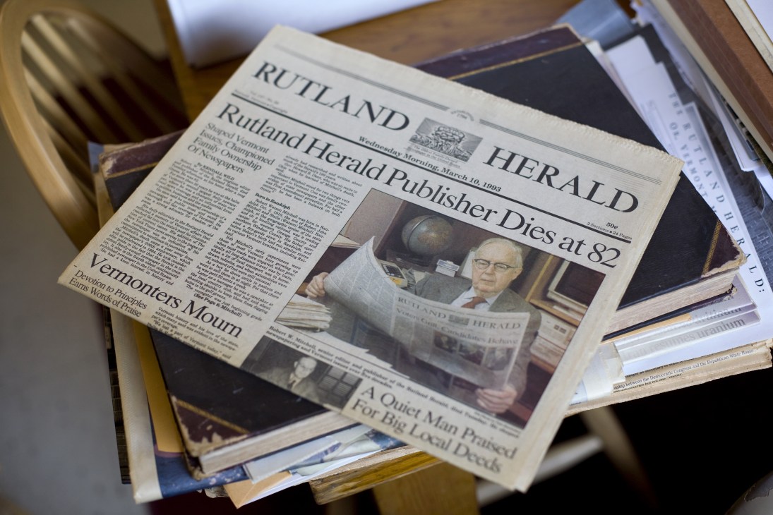 Rutland Herald newspaper front page with headline about publisher's death, showing archival copies stacked together.