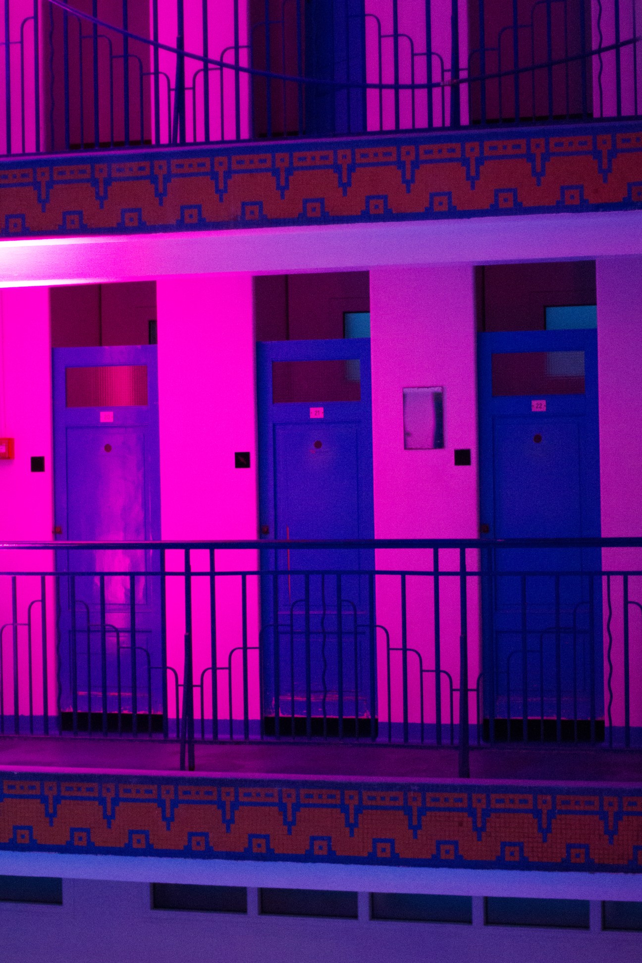 Neon-lit interior of La Piscine de Pontoise changing rooms with magenta and blue illumination across two floors.