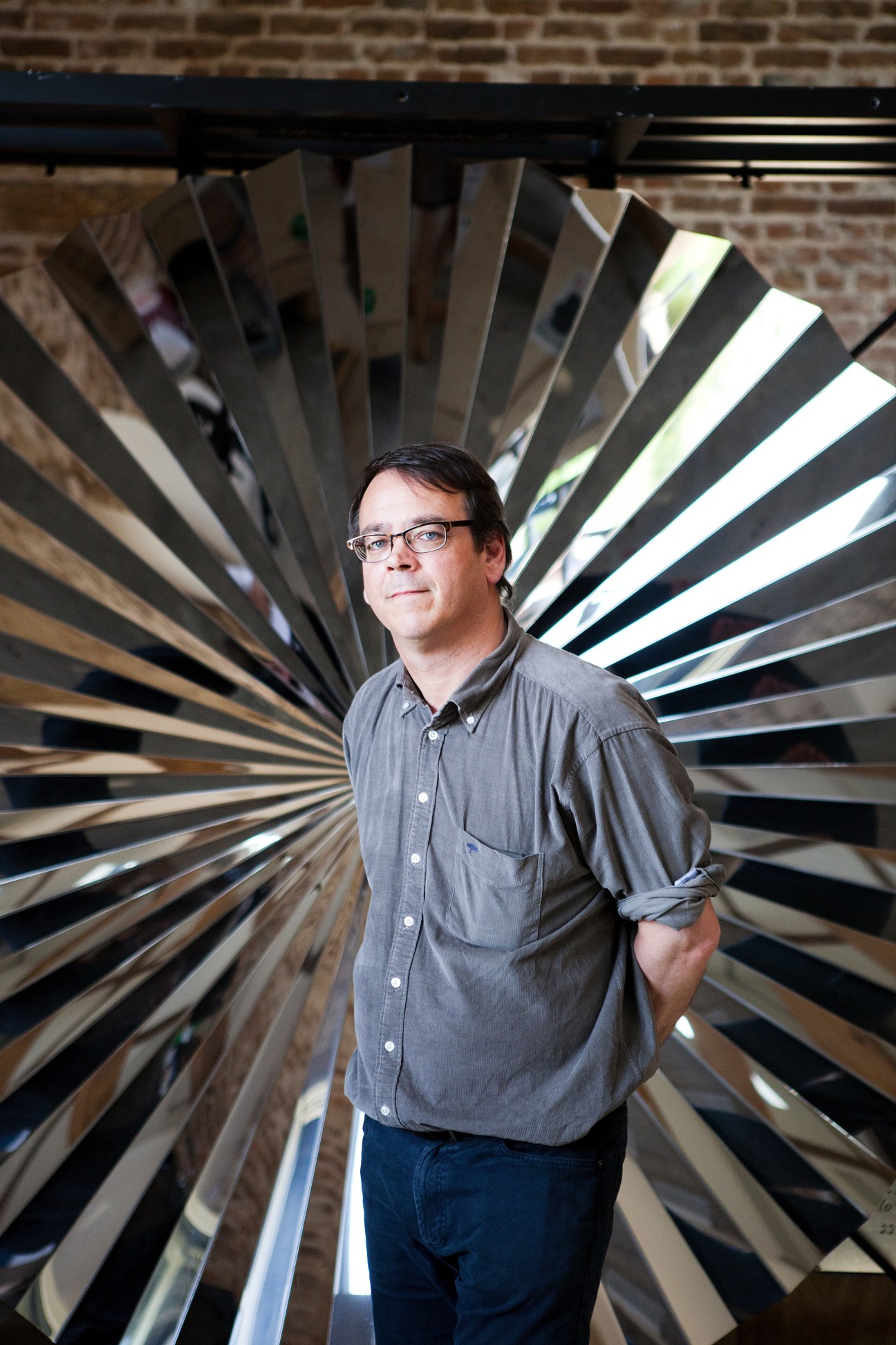 Andrew Ignarski stands in front of a reflective mirrored Anish Kapoor sculpture with radiating metallic panels.