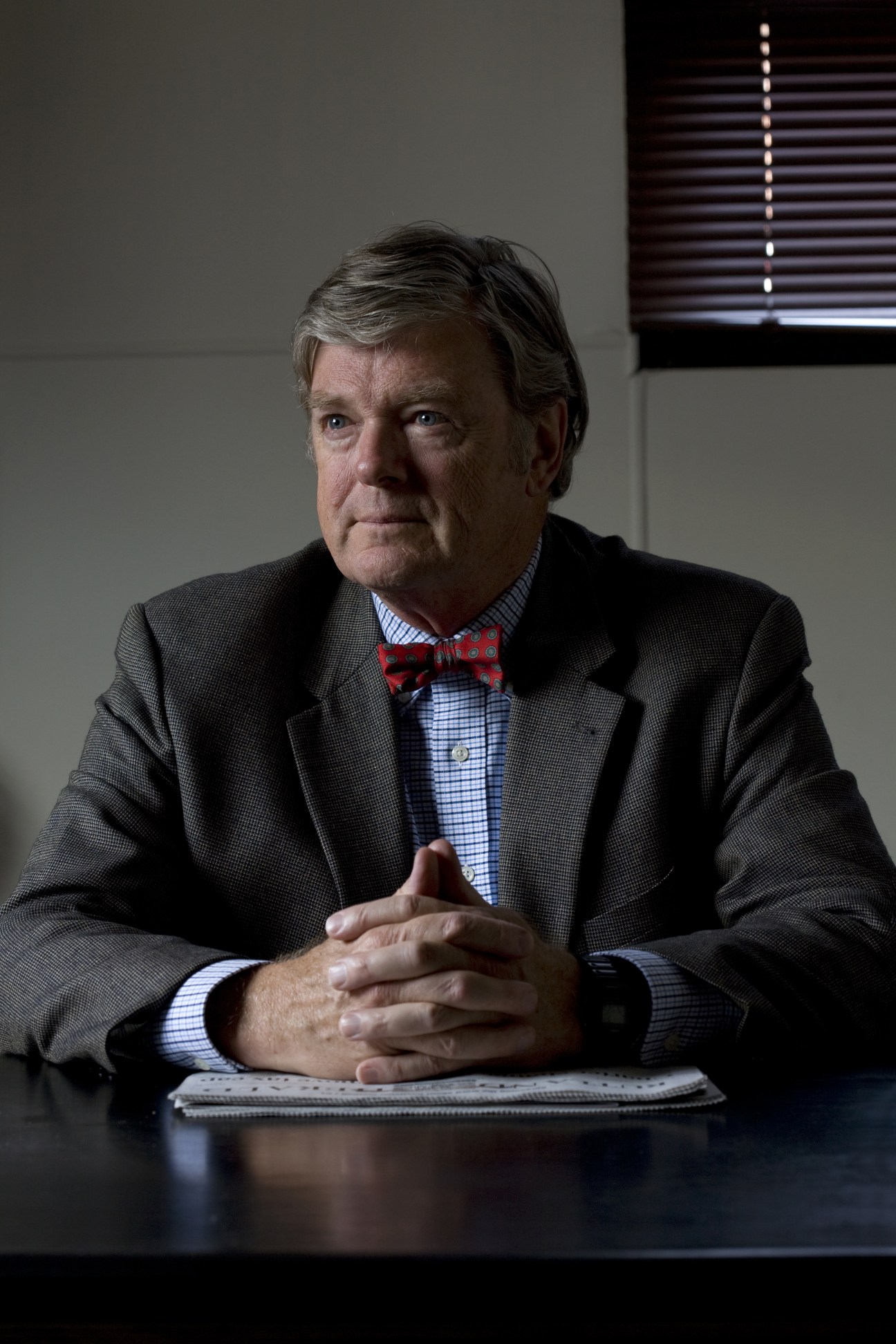 R John Mitchell, publisher of the Rutland Herald, wearing a red bow tie and grey blazer at his desk.