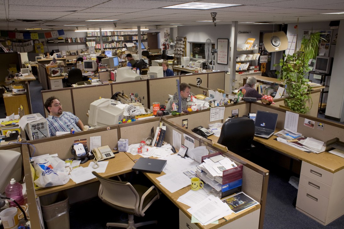 Rutland Herald newsroom with cubicles, desks, computers, papers, and staff members working at various stations.
