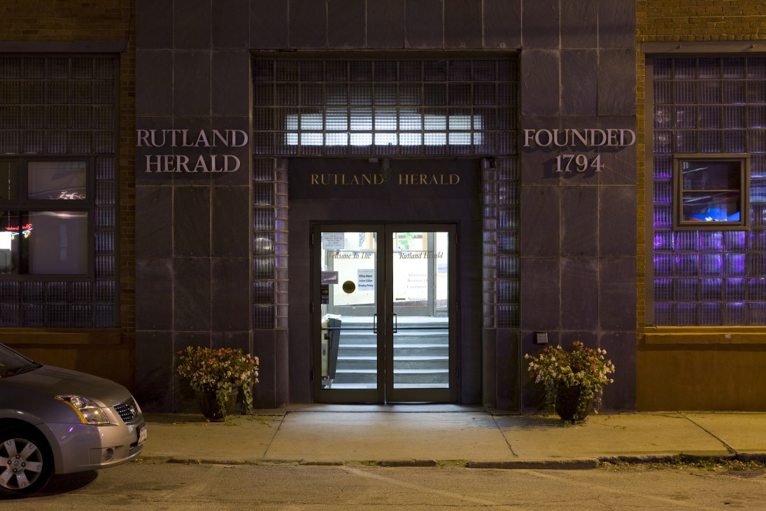 Rutland Herald newspaper office entrance at night, displaying 'Founded 1794' on dark facade with glass doors.