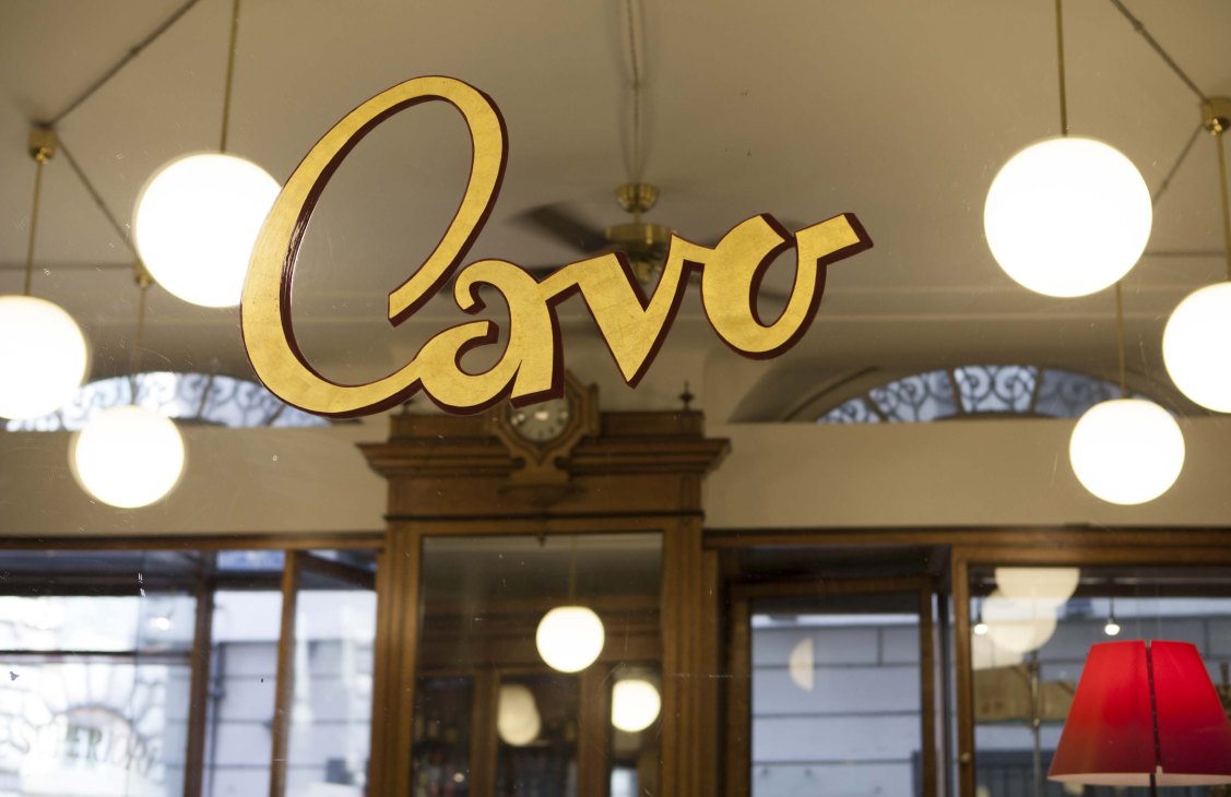 Golden cursive lettering spelling 'Cavo' mounted on storefront with illuminated circular lights