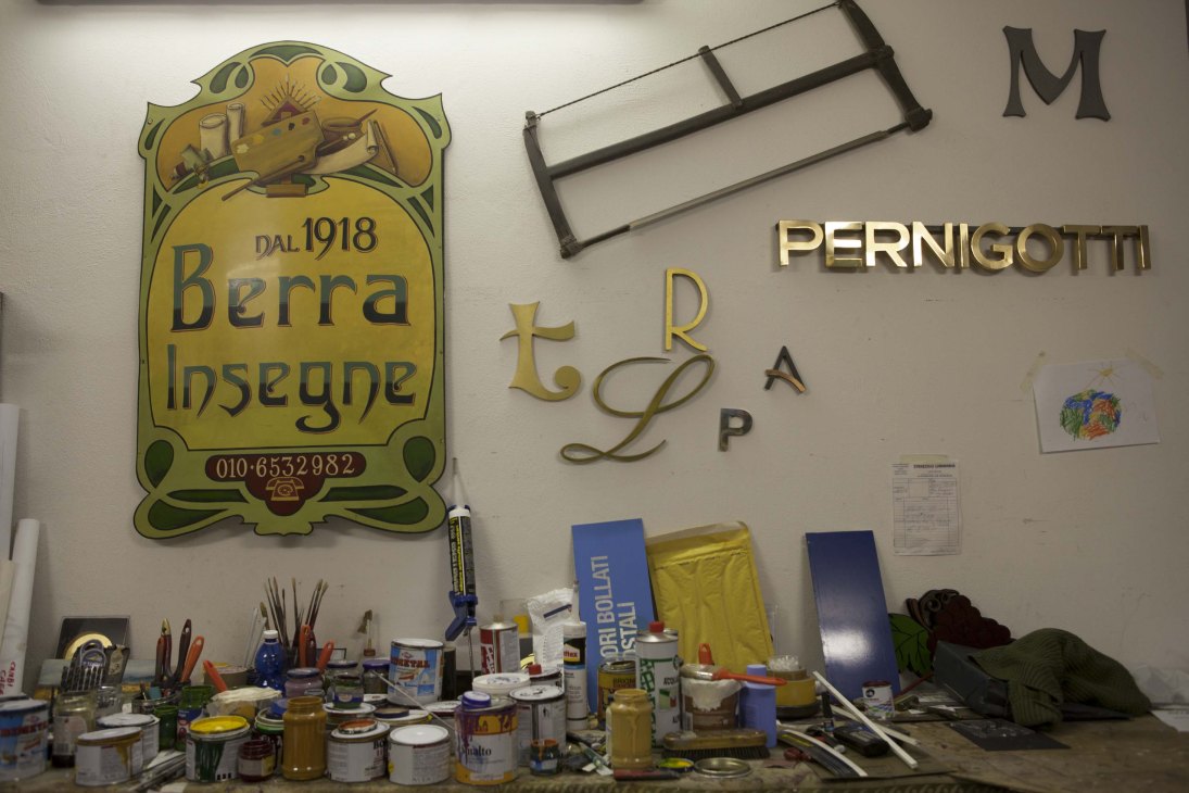 Workshop wall displaying vintage signage including an ornate yellow art nouveau sign reading 'Berra Insegne' dated 1918 and brass letters spelling 'PERNIGOTTI'.