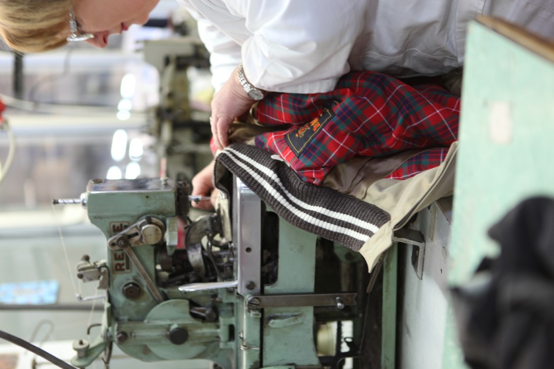 Worker operating industrial knitting machine to produce striped fabric for Baracuta clothing in Milan factory.