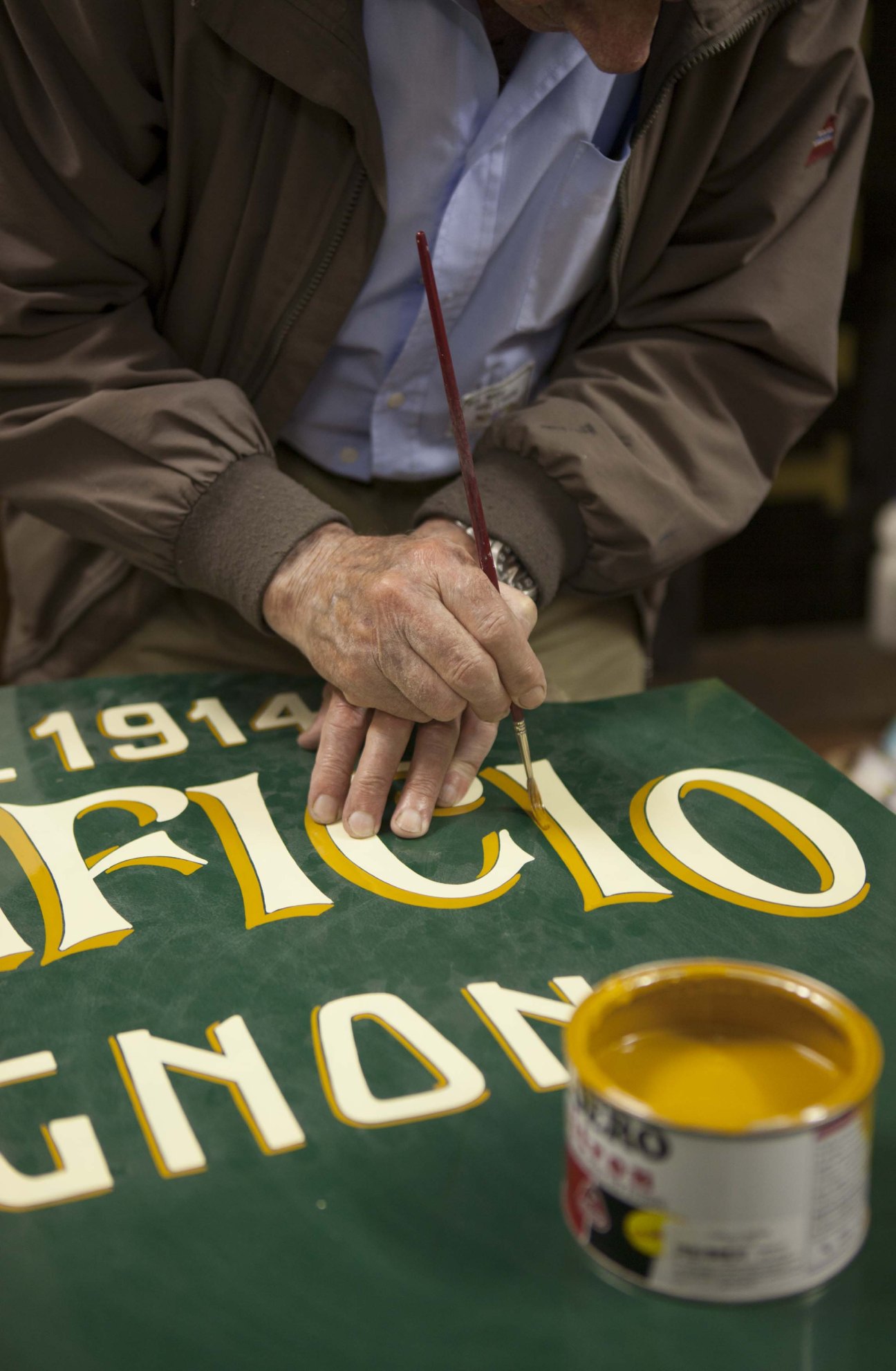 Elderly signmaker Alberto Berra paints shading on a large gold and cream letter with a fine brush.
