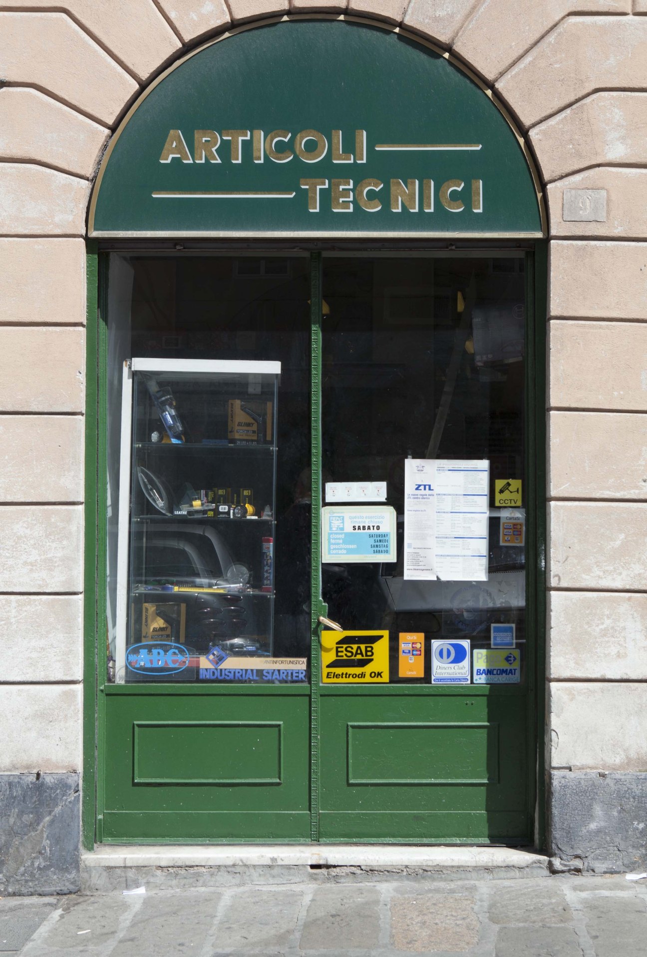 Green storefront with arched top displaying gold-leaf lettering reading 'Articoli Tecnici' on dark teal background.