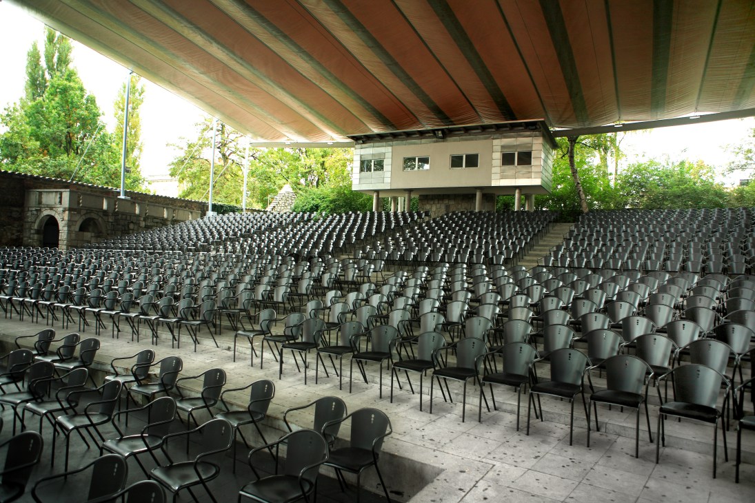 Empty black chairs arranged in rows under a retractable canopy at an outdoor amphitheater venue.