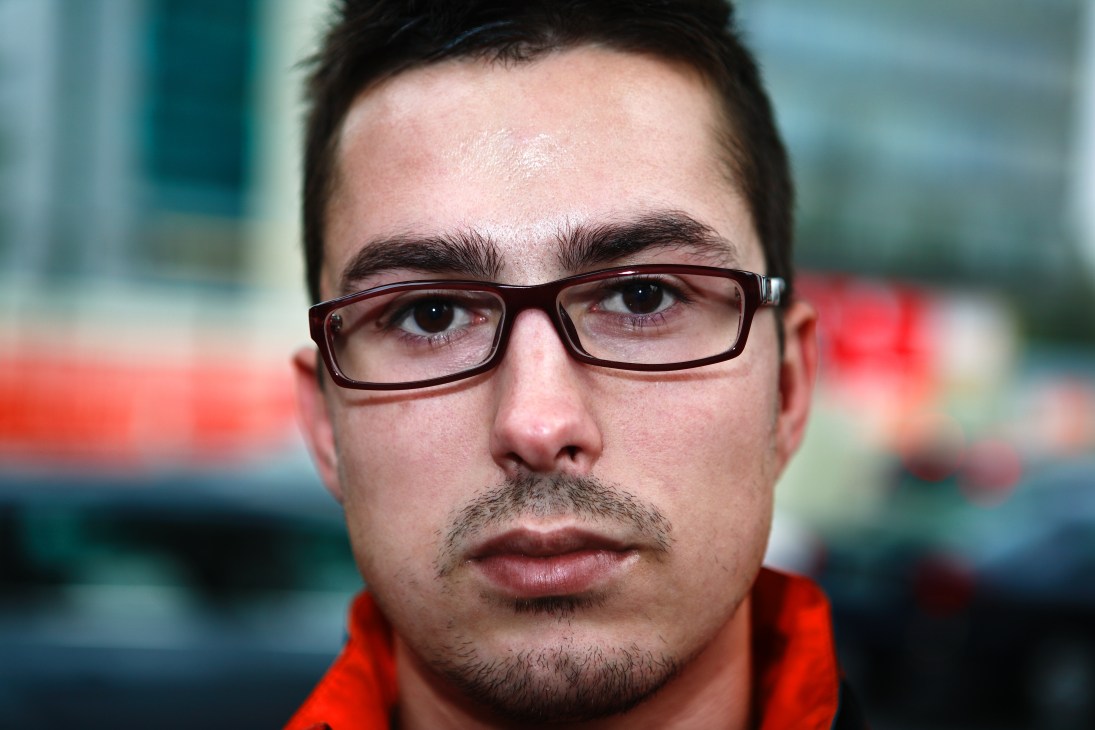 Portrait of a young man wearing glasses and a red jacket against a blurred background.