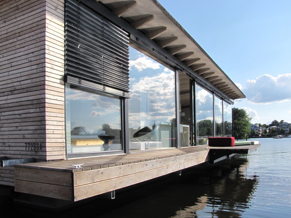 Modern waterfront boathouse with large glass windows, wooden deck, and red seating platform extending into the lake.