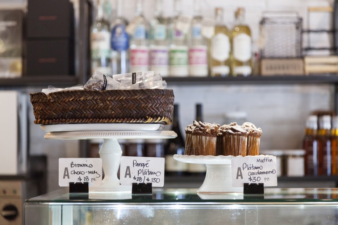 Bakery display counter at Abarrotes with cakes and pastries on white pedestals with handwritten price labels.
