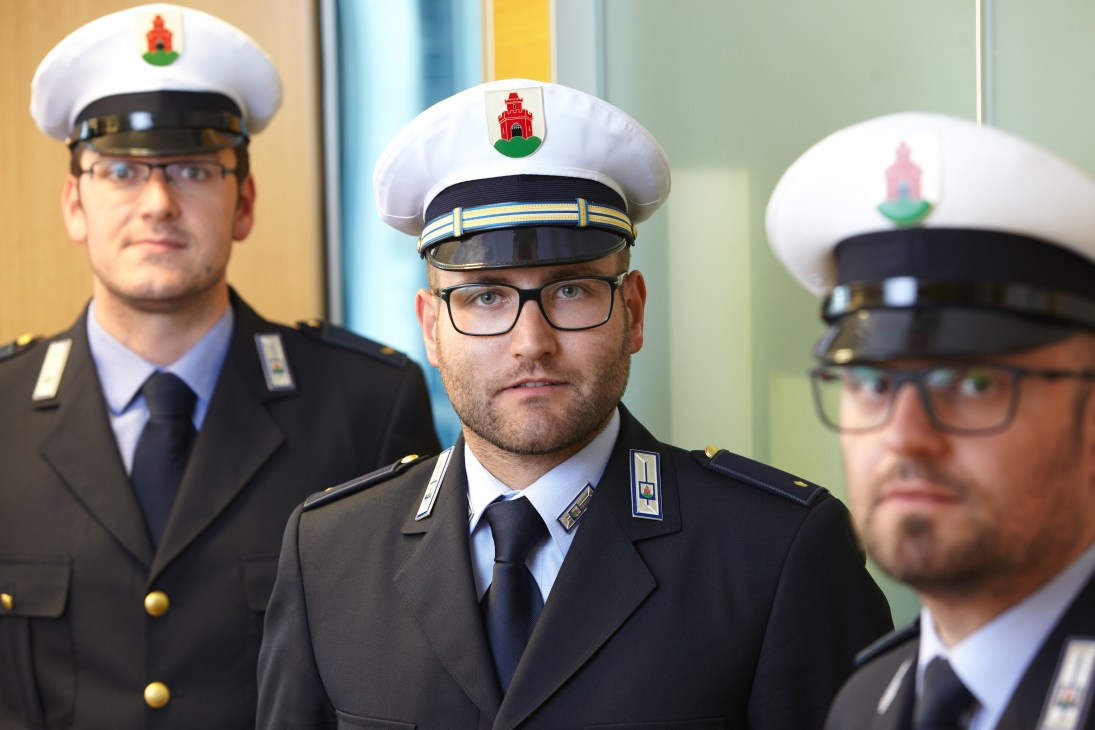 Three Italian police officers in formal uniforms with white caps and emblems stand in an official interior setting.
