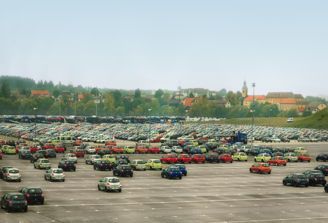 Hundreds of colorful Renault vehicles parked in rows at an industrial lot with a European village in the background.