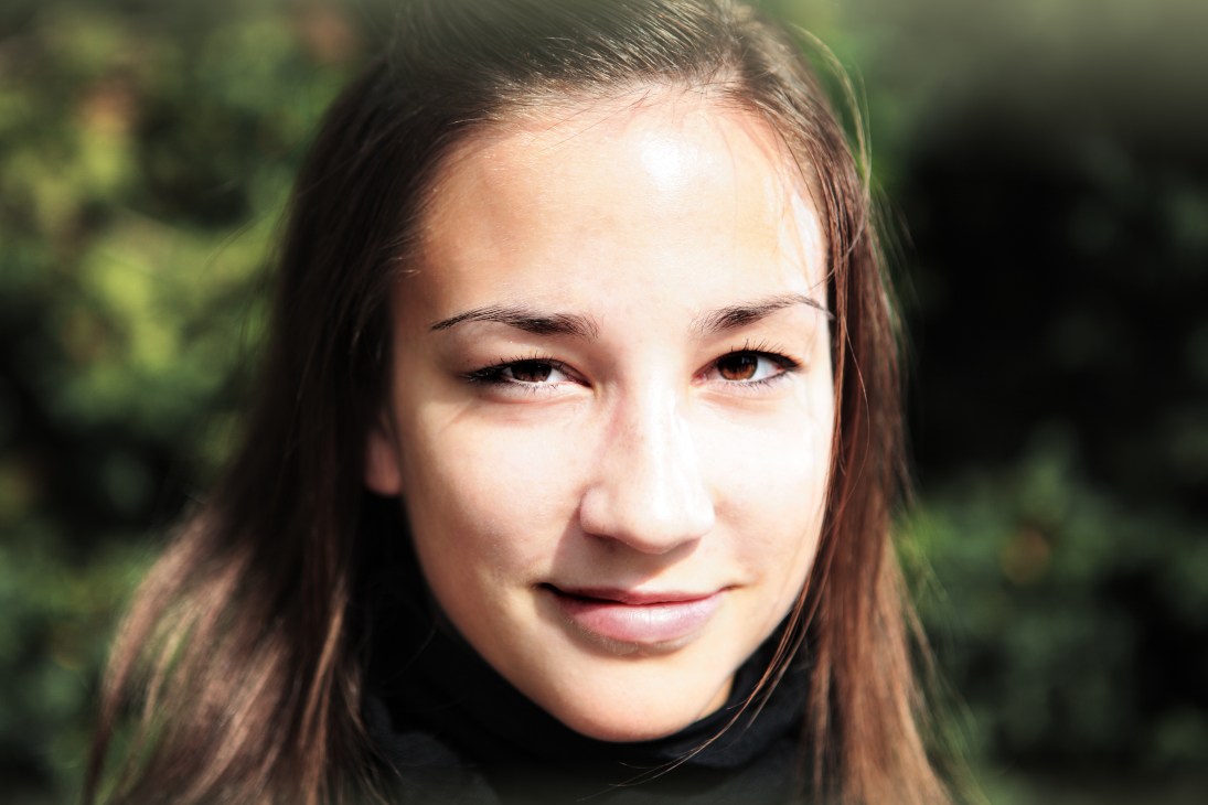 Eva Koprišek, 19-year-old student from Ljubljana, smiling outdoors with blurred green foliage background.