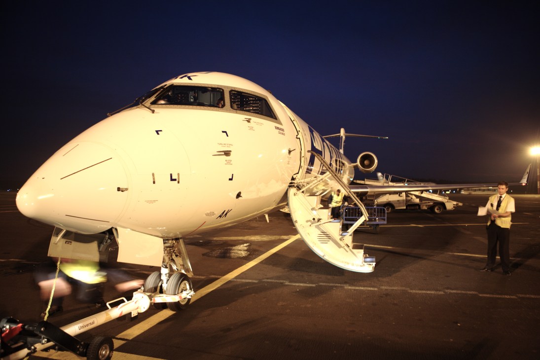 An Adria Airways passenger jet parked on the tarmac at night with ground crew nearby.
