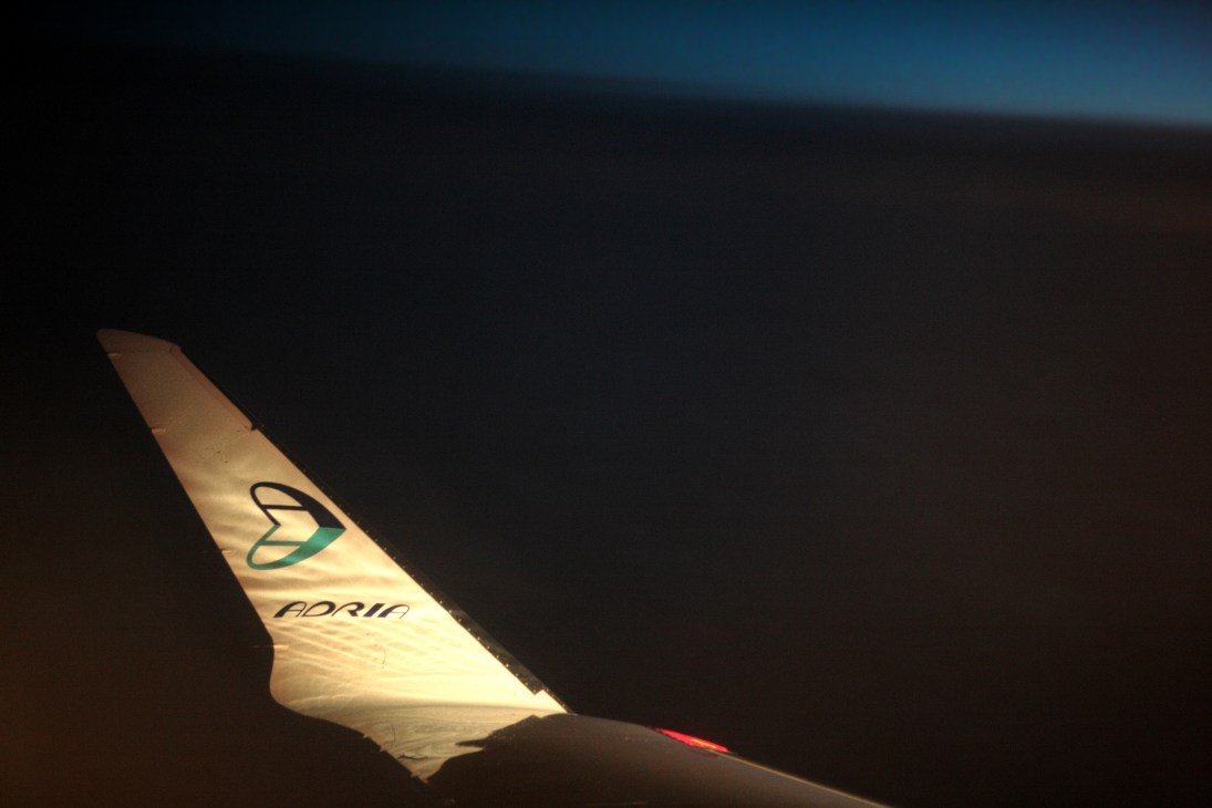 Adria Airways aircraft tail fin with airline logo illuminated at dusk or dawn.