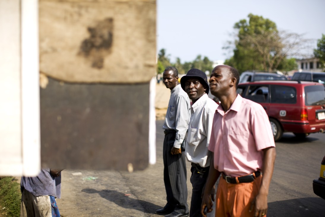 Men stand reading the Daily Talk blackboard newspaper on a Monrovia street.