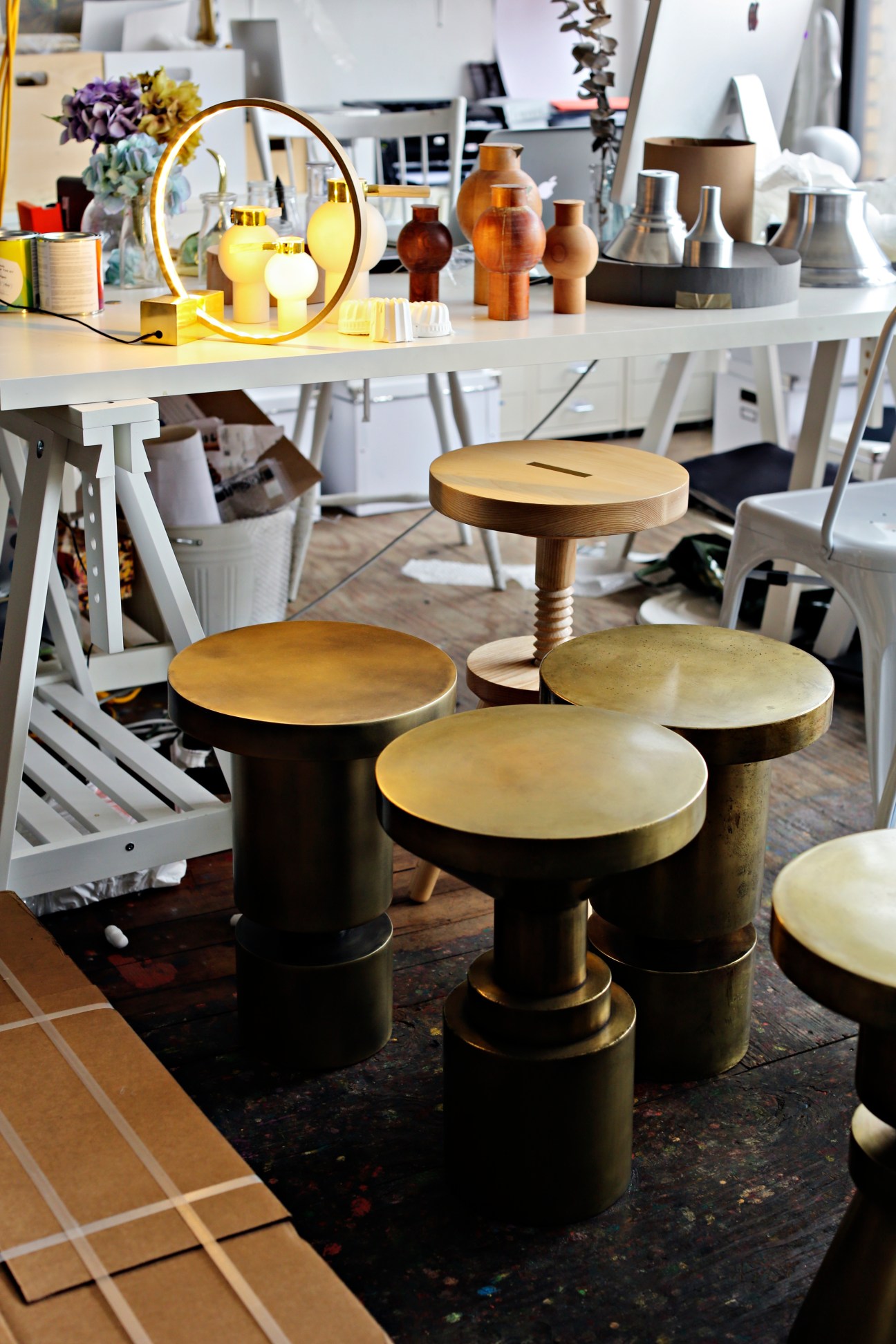 Design studio display featuring brass and black cylindrical tables with brass tops and a brass ring lamp.