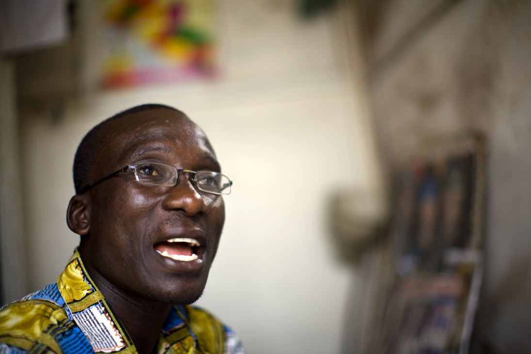 Portrait of Alfred Sirleaf, founder of Daily Talk blackboard newspaper, wearing glasses and a yellow and blue patterned shirt.
