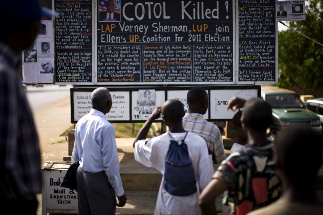 Readers gather around Alfred Sirleaf's blackboard Daily Talk newspaper in Monrovia to read chalked headlines.