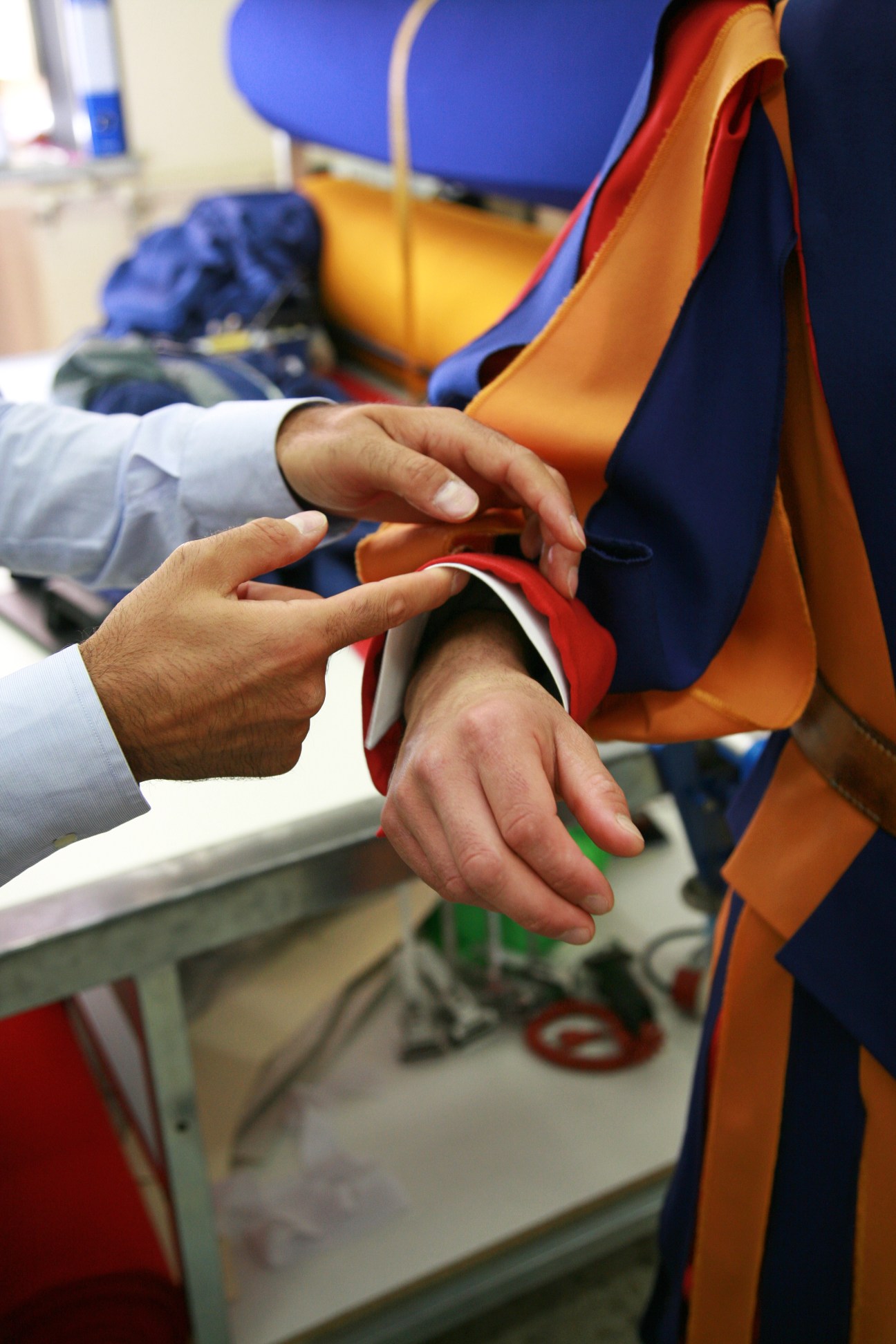 Tailor's hands inspecting the collar of a Swiss Guard uniform with blue, yellow and red stripes.