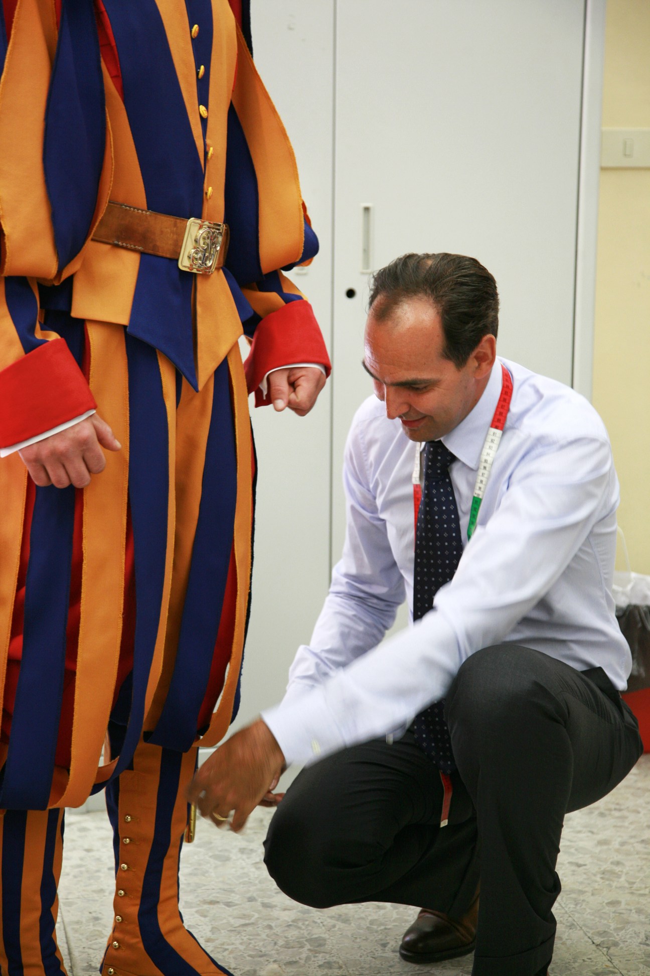 Tailor Ety Cicioni crouches to button a Swiss Guard's red gaiter on their striped uniform.