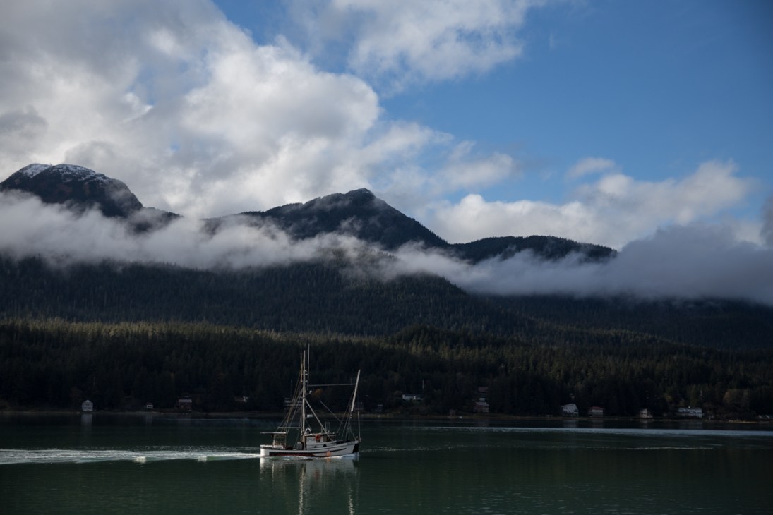Fishing vessel Sitkoh motoring through Gastineau Channel with forested mountains and mist in background.