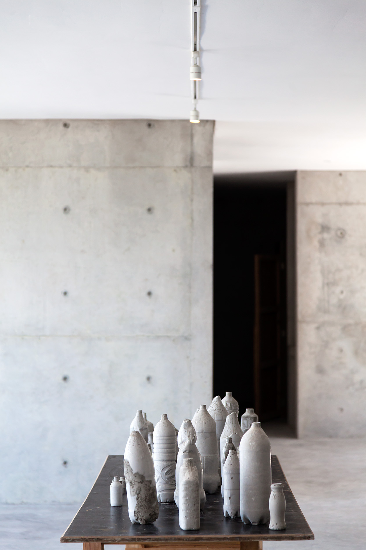 White ceramic vessels arranged on a dark platform in a minimalist gallery space with concrete walls.