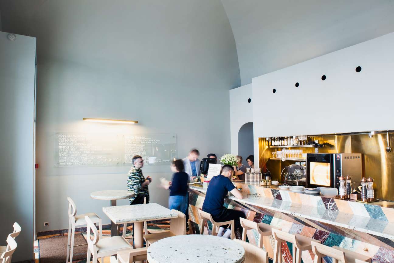 Interior of Iskra café in Moscow with curved white walls, brass counter, and customers ordering at the service counter.