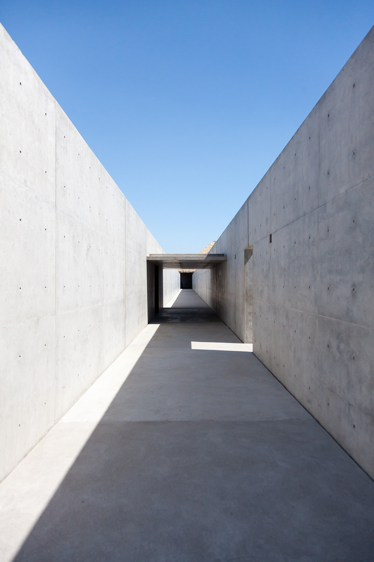 A concrete corridor with high walls connecting studios to the main villa at Casa Wabi artist residency.
