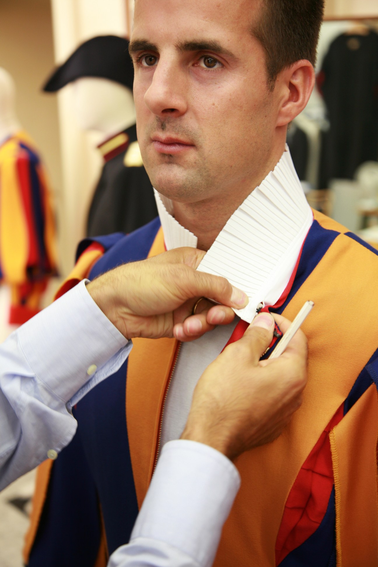 A tailor buttons the white plissé collar on a Swiss Guard's blue and yellow striped dress uniform.