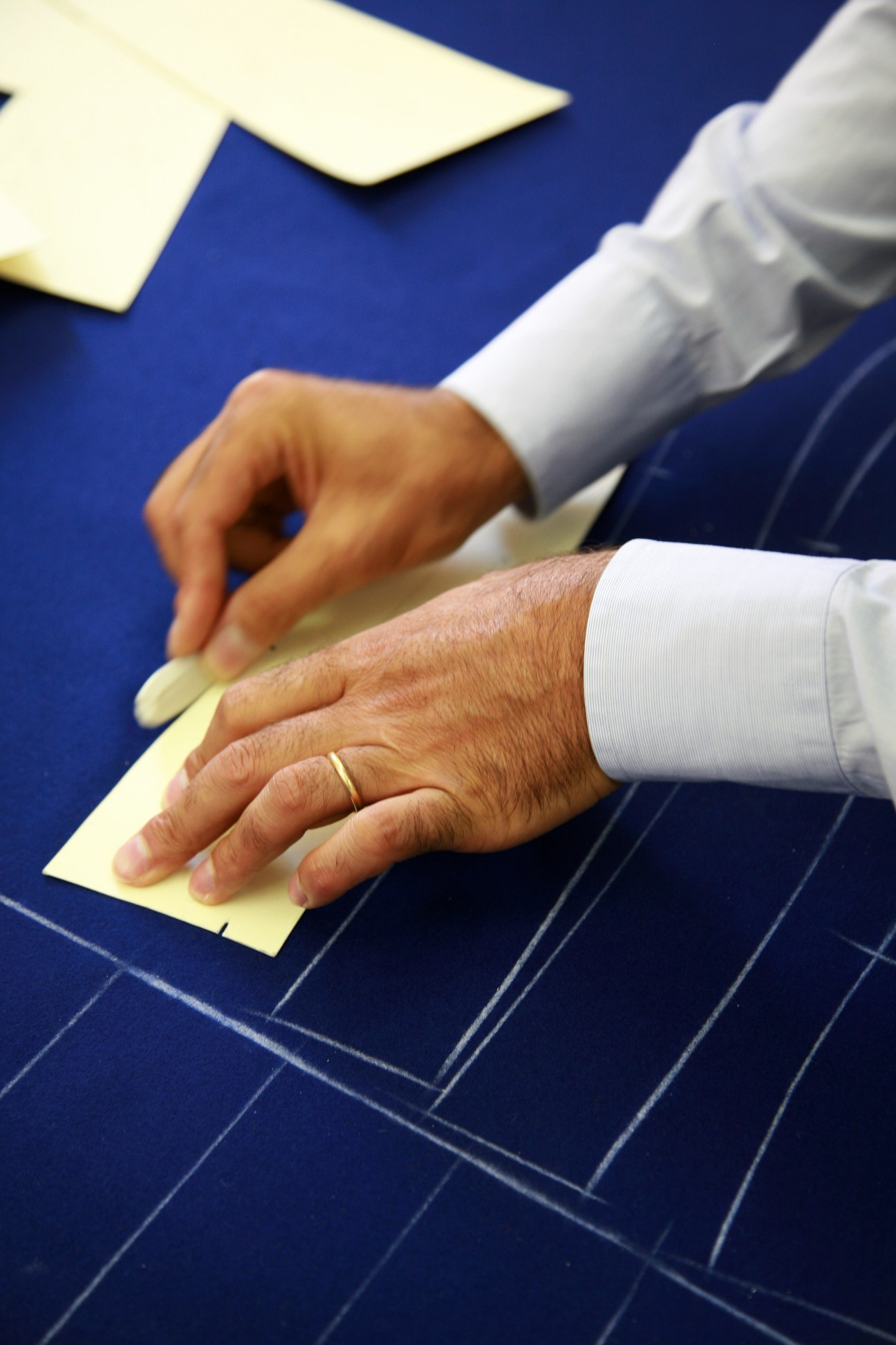 A tailor's hands outlining a pattern with chalk on blue fabric with white pinstripes.