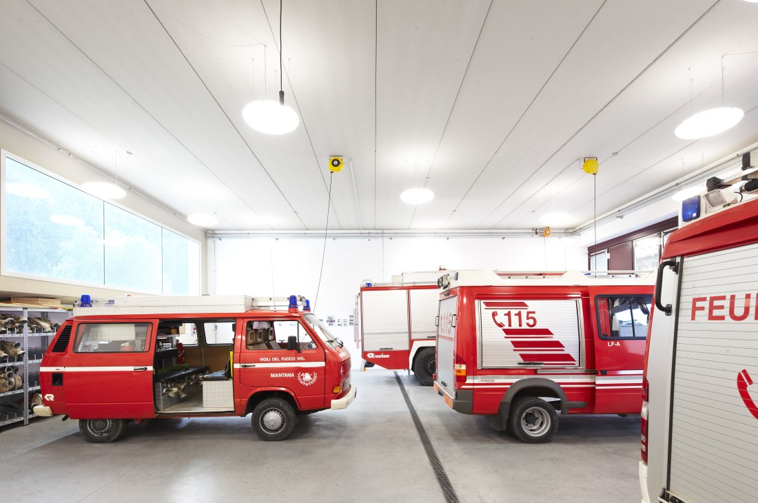 Red fire trucks parked inside a modern white fire station with minimalist design in Mantana, South Tyrol.