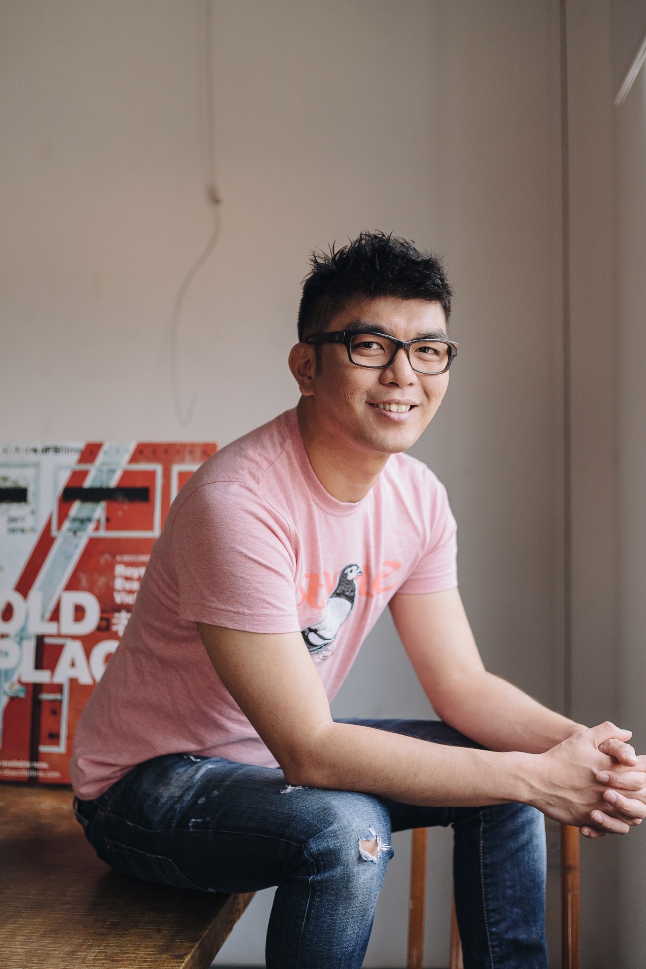 Director Royston Tan wearing glasses and a pink T-shirt, smiling at the camera in an indoor setting.