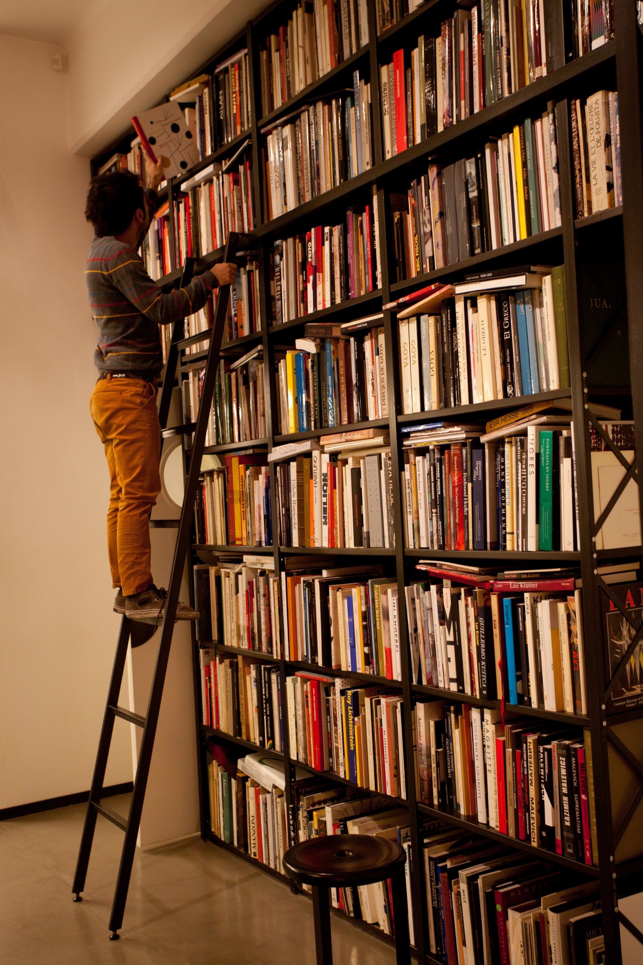 Gallery employee Ramiro Smith Estrada on a ladder organizing books on a tall wooden bookshelf.