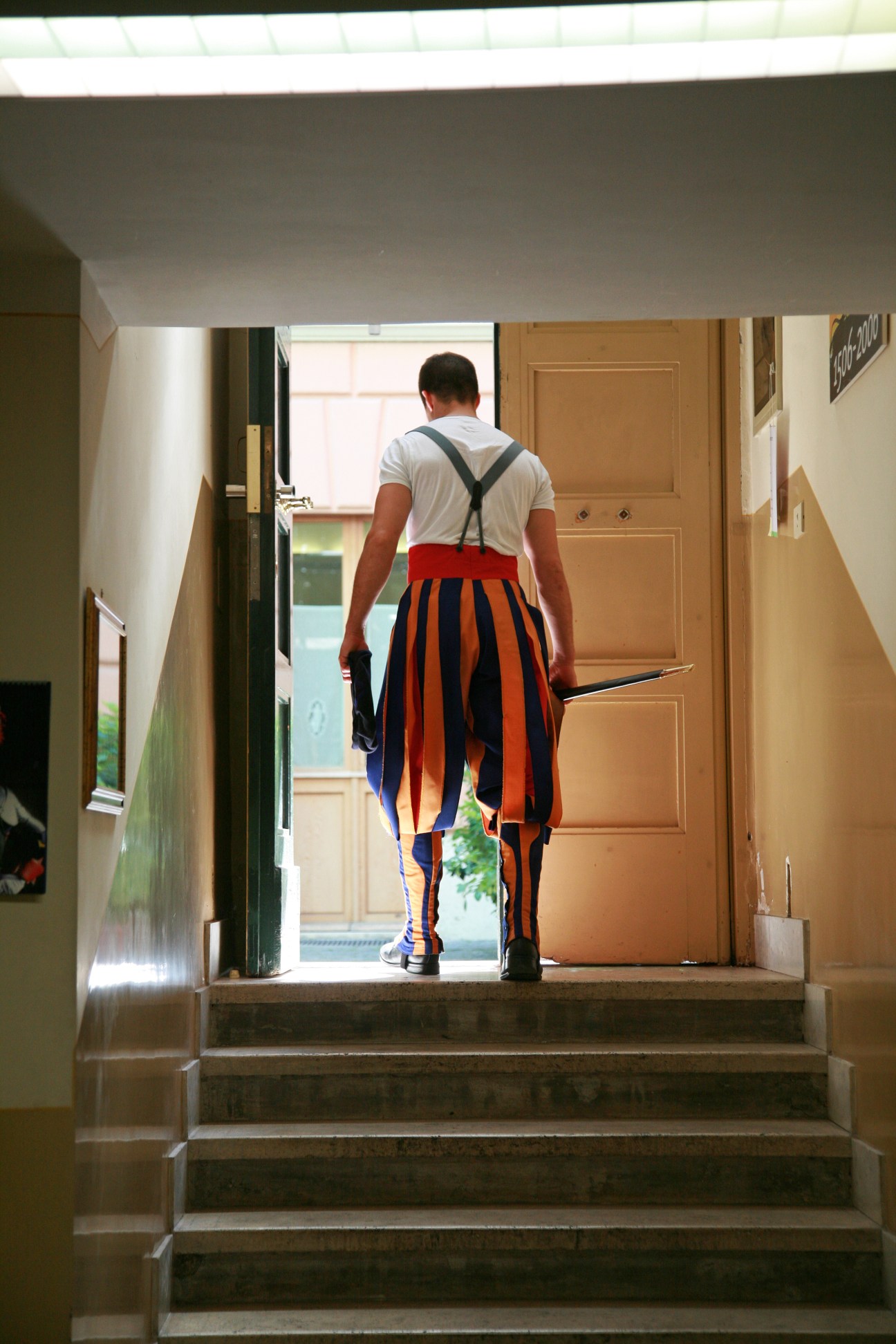 Swiss Guard in barracks wearing striped blue and red dress uniform with halberd walking down corridor